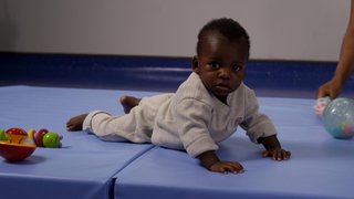 A baby raises themselves on a mat using their arms.