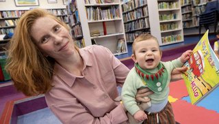 A woman and her baby. The baby is holding a storybook in his hand.