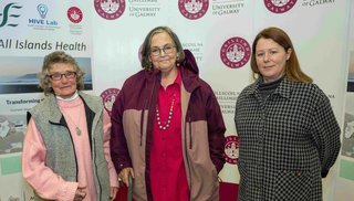 Three women standing in front of pull up banners reading "All Islands Health" and "University Hospital Galway"