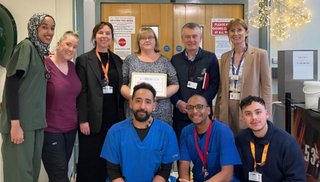 A group of healthcare workers smiling into the camera. One woman is holding a certificate