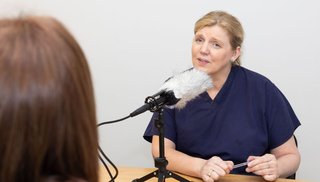 A woman speaking sitting at a table, talking into a microphone