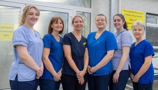 A group of healthcare workers wearing scrubs smiling into camera