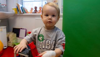A boy in a hospital setting. He's wearing a bandage on his hand.