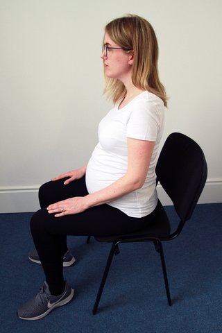 Image of woman sitting straight on a chair with her arms out forward on her knees
