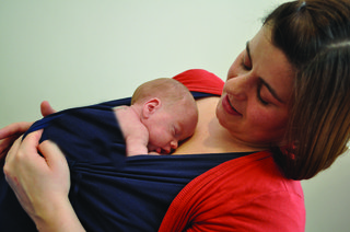 A mother holds her premature baby on her chest with a blanket going across the baby's back