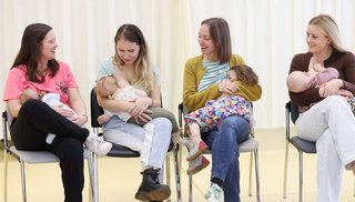Four women sitting holding babies in their arms.