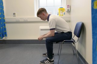 Physio sitting on chair leaning forward resting his elbows on his knees