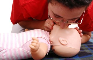 First aider demonstrating rescue breaths on an infant CPR dummy. They have their mouth sealed over the dummy's mouth and nose to blow in