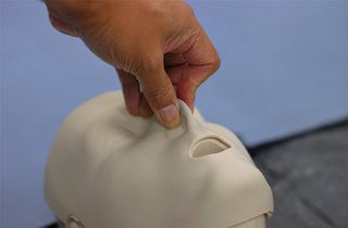 First aider pinching the nose of a CPR dummy. They have a thumb and finger on each side of nose, pinching it closed.