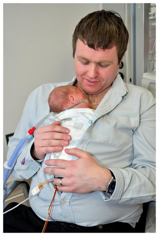 A father holds his premature baby on his chest underneath his shirt