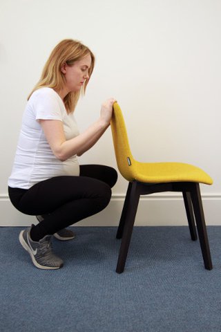 pregnant woman doing a squat while holding the back of a chair