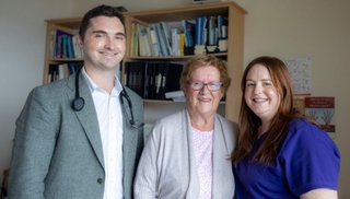 Two women and a man standing. The man has a stethoscope around his neck.