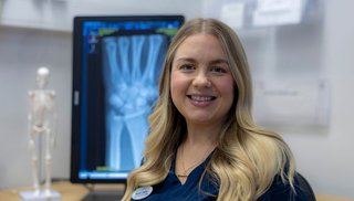 Woman stands in front of large xray image screen and smiles at the camera