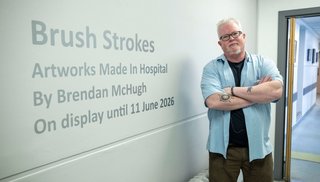 Man stands with arms folded beside a wall that has the words Brush Stokes written on it.