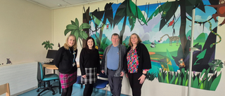Group of four adults standing and smiling at the camera in front of a colourful mural