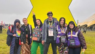 Group of six young adults, smiling, in the rain at a festival