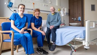 Two healthcare workers sitting on chairs beside a man sitting on a hospital bed