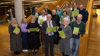 15 people holding yellow booklets and smiling at the camera