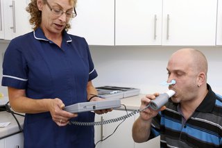 Man doing a spirometry test. He has a soft clip on his nose and is blowing into a mouthpiece.