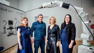 Three women and one man standing next to a robotic-assisted healthcare equiptment