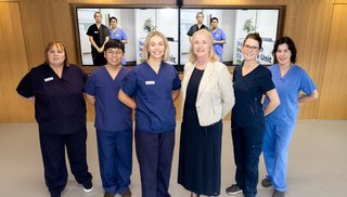 A group of healthcare professionals standing with two screens behind them