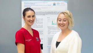 Two female healthcare workers standing in front of a poster