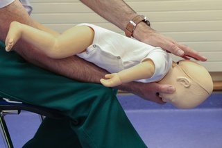 First aider demonstrating back thrust with an infant CPR dummy