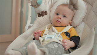 A baby sitting in a baby bouncer with a 5-way safety harness