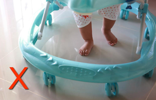 A baby standing up in a baby walker, with a red cross in the corner of the picture