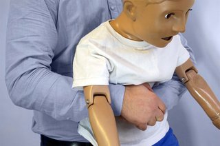 First aider demonstrating abdominal thrusts with a child CPR dummy