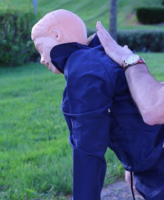 First aider slapping a child CPR dummy between the shoulder blades