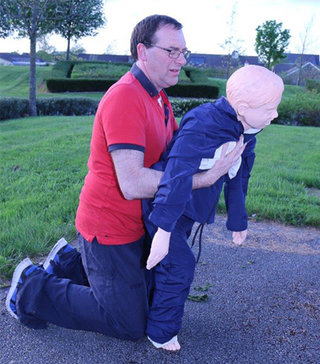 First aider demonstrating the forward-leaning position with a child CPR dummy