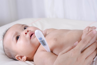 Baby lying on cot with thermometer under its arm