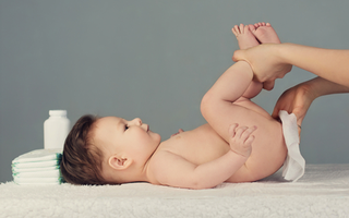 A baby lying down and a parent wiping their bum