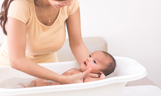 Lift your baby into the water with one arm behind their shoulders and neck, holding their outside arm with your hand.