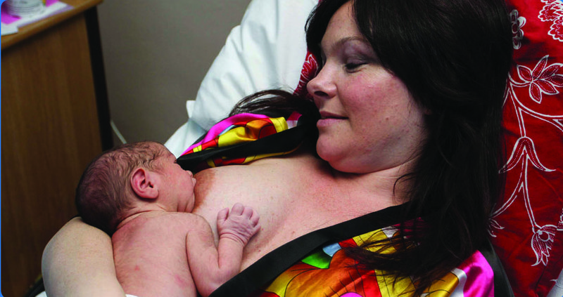 Woman lying down with a baby on top breastfeeding