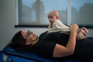 A woman lying on her back  with a baby on her chest.
