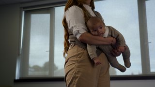 A woman carrying a baby head-down supported by her arm.
