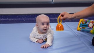 A woman plays with her baby, dangling a toy above them.
