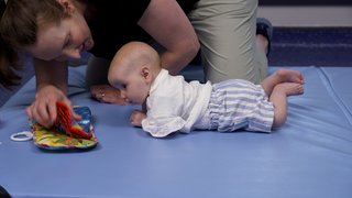 A woman plays with her baby and toys on a mat.
