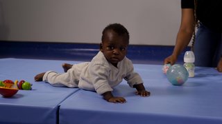 A baby raises themselves on a mat using their arms.