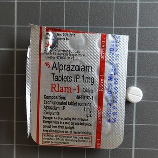 The back of a counterfeit alprazolam blister pack next to a small white tablet. Rlam-1 is written on the foil label.